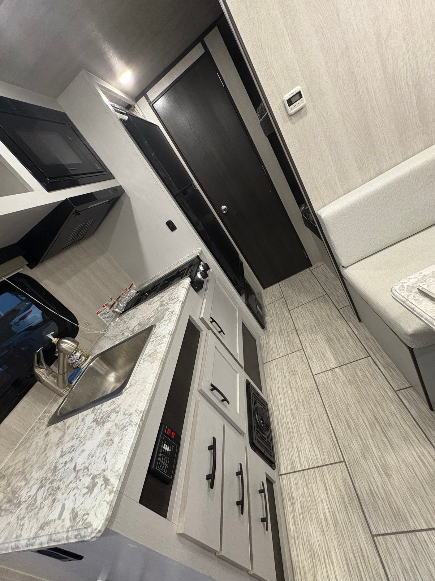 Modern RV rental kitchen with sink, microwave & stovetop, next to a comfy dinette area. Light, bright interior.
