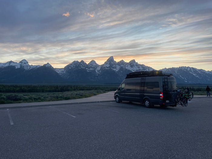 Grand Teton mountains & landscape at sunset/sunrise with an RV rental camper van, bikes on back.