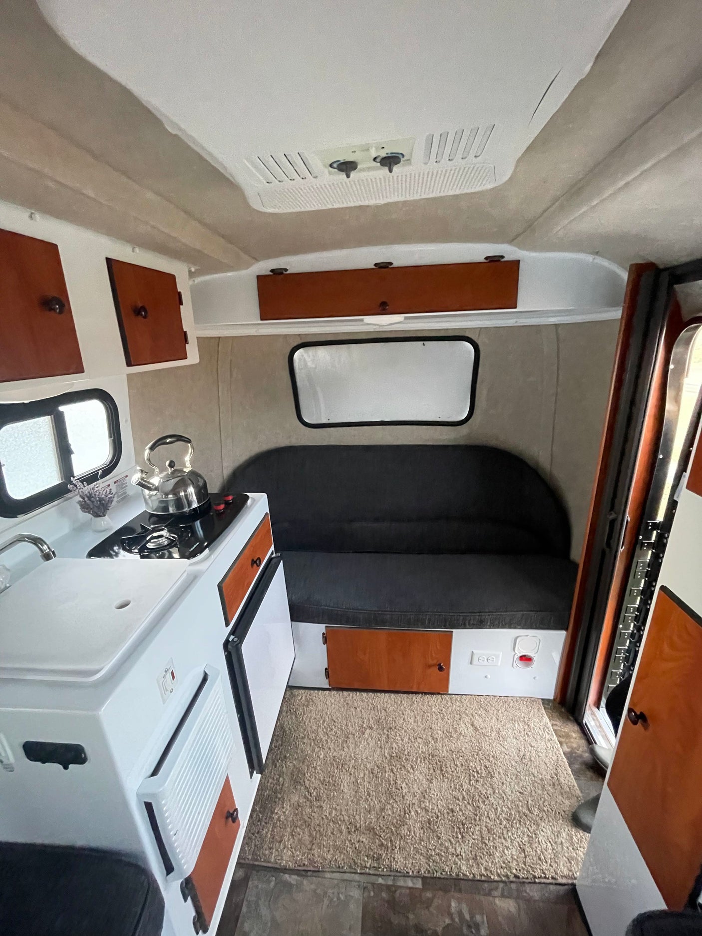 This cozy rv rental interior features a compact kitchenette with stove and sink, a sofa bed, wood cabinets, and AC.