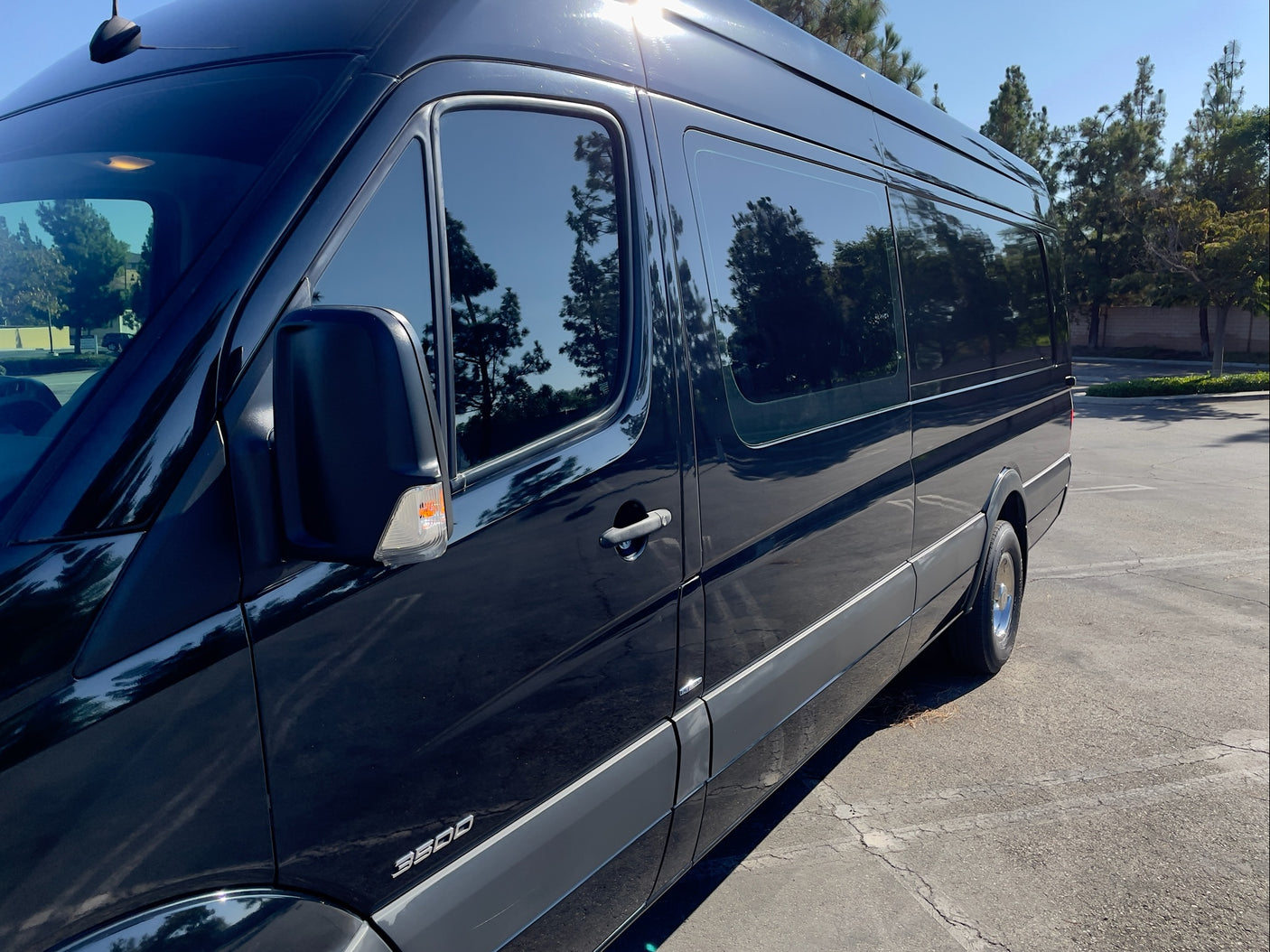 Black Sprinter van side profile, ready for your RV rental journey. Tinted windows reflect surrounding trees and sky.
