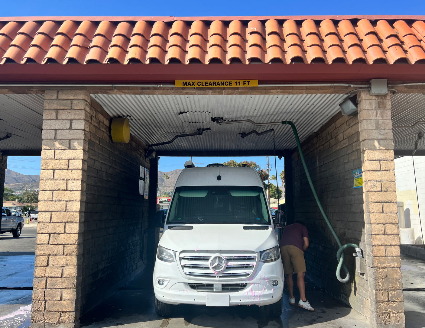 An RV rental van is being hand-washed in a self-service car wash bay, with a 'MAX CLEARANCE 11 FT' sign overhead.