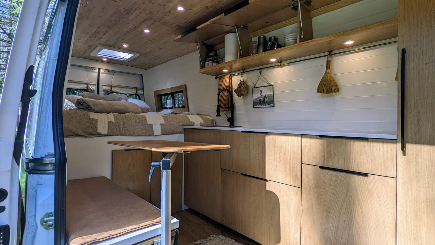 Spacious custom RV rental interior features a comfortable bed, kitchen, dining table, and smart storage for van life.