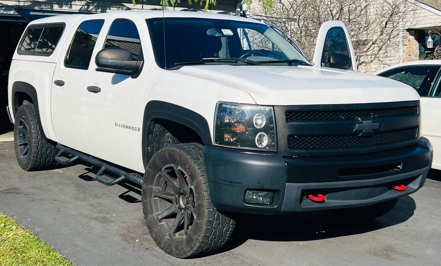 White Chevrolet Silverado pickup truck with a white camper shell, resembling a compact RV rental, parked on an asphalt driveway.