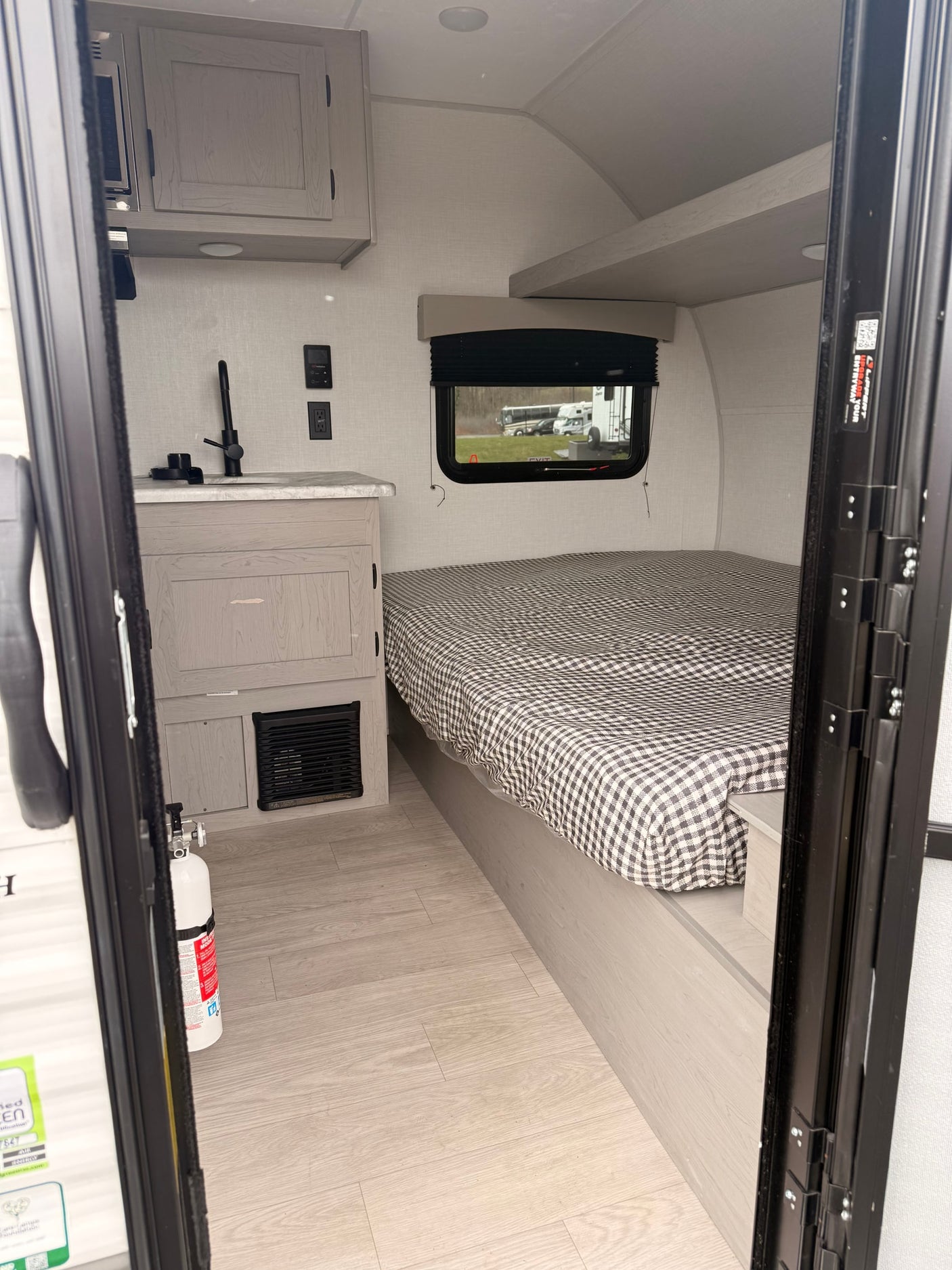 Step into this modern RV rental: a compact interior with a checkered bed, functional kitchen, and light wood floors.