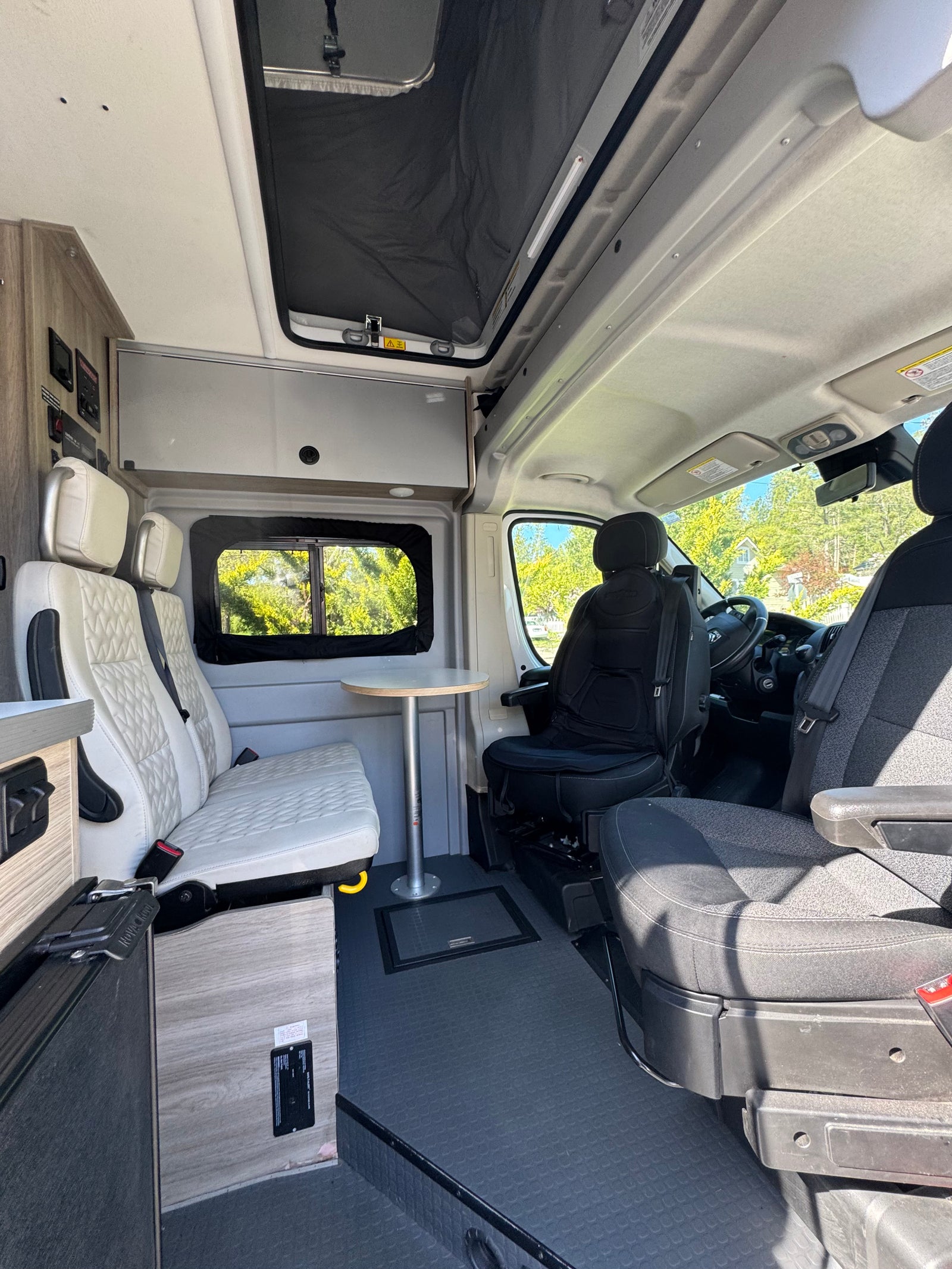 Modern rv rental interior with white quilted passenger seats, dining table, and driver's cabin.