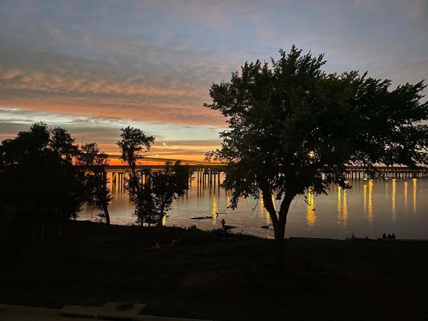 Golden sunset over a lake, bridge lights shimmer. Perfect peaceful stop on your RV rental journey.