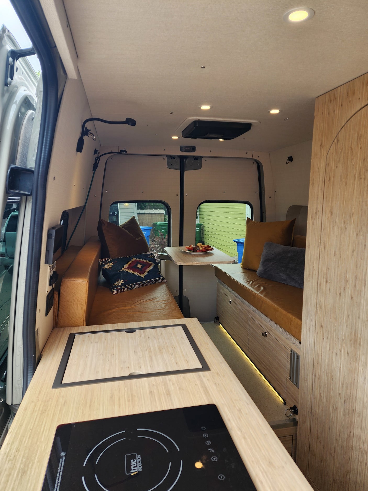 Modern camper van RV rental interior: kitchen with induction, cozy seating, and a dining table.