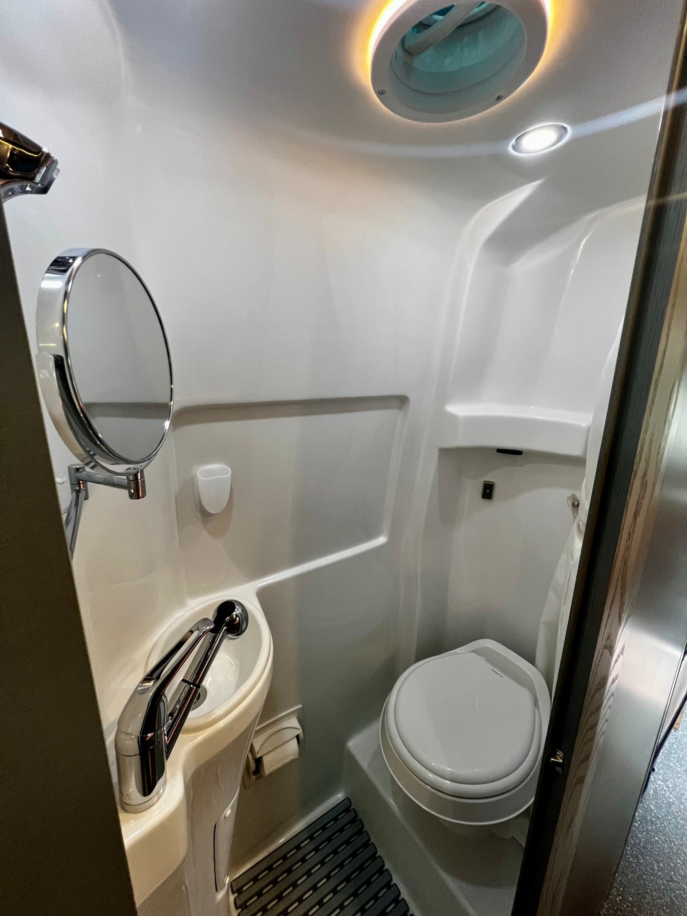 Functional RV rental bathroom featuring a compact toilet, sink with mirror, and an integrated shower area.