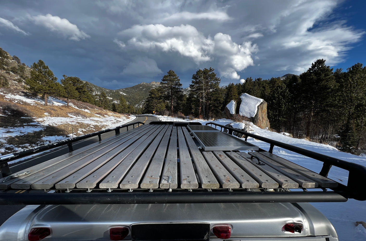Winter rv rental journey through snow-covered mountains, featuring a roof rack & solar panels under dramatic skies.