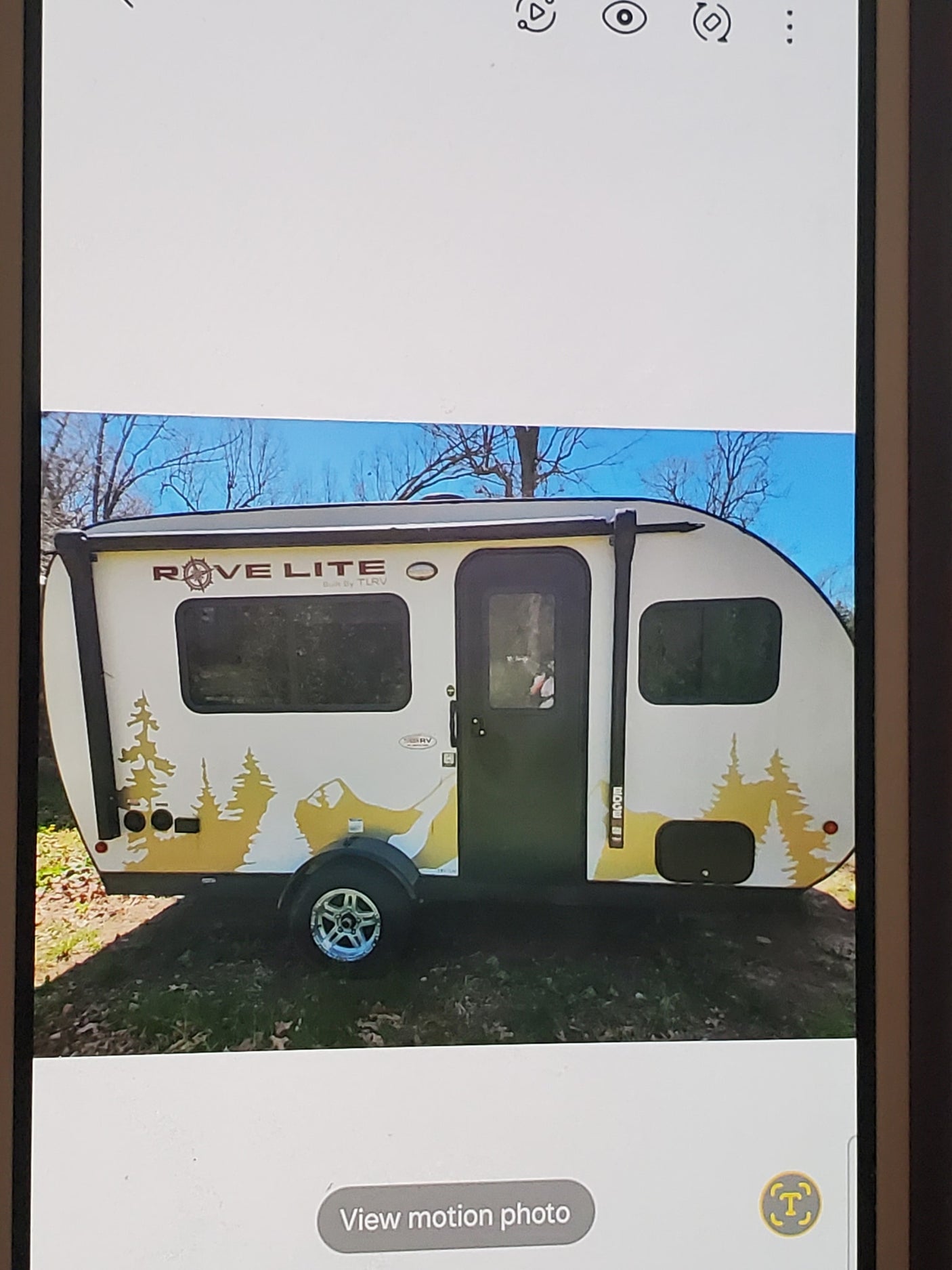 White Rove Lite teardrop RV with yellow forest graphics, parked outdoors. Ideal RV rental for your next adventure.