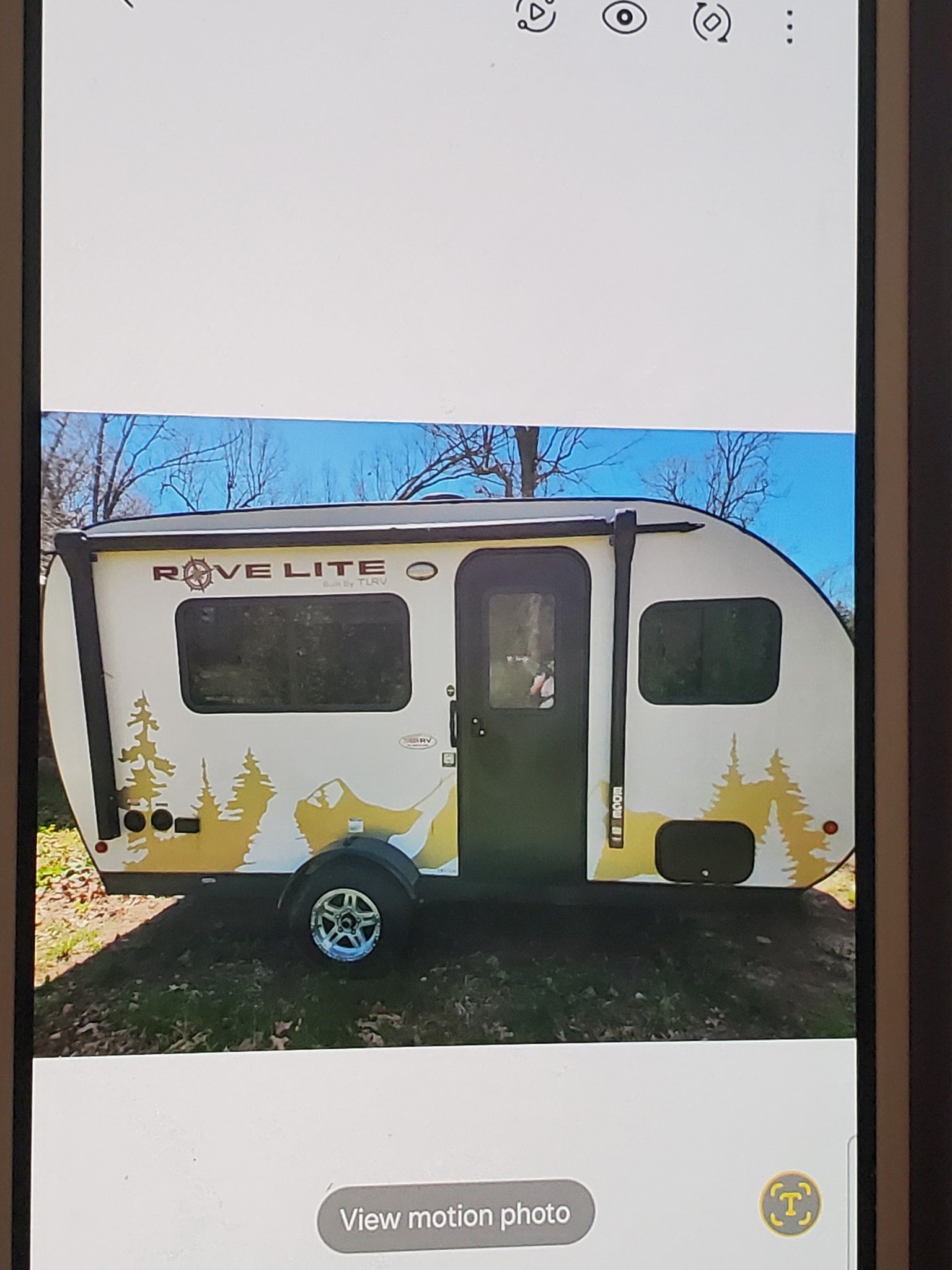 White Rove Lite teardrop RV with yellow forest graphics, parked outdoors. Ideal RV rental for your next adventure.