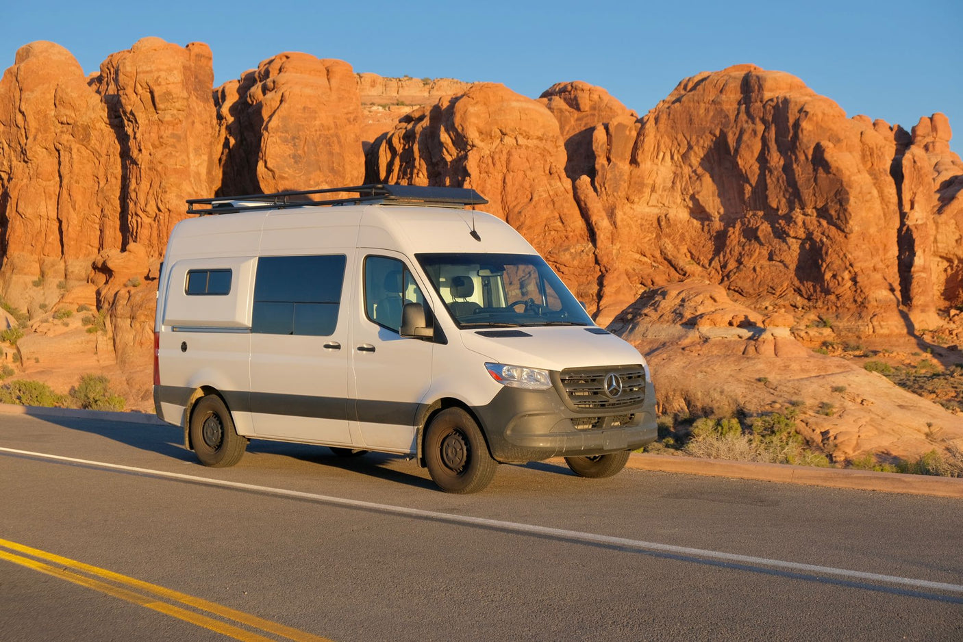 White Mercedes Sprinter RV rental on a road through red rock desert. Explore stunning landscapes by camper van.