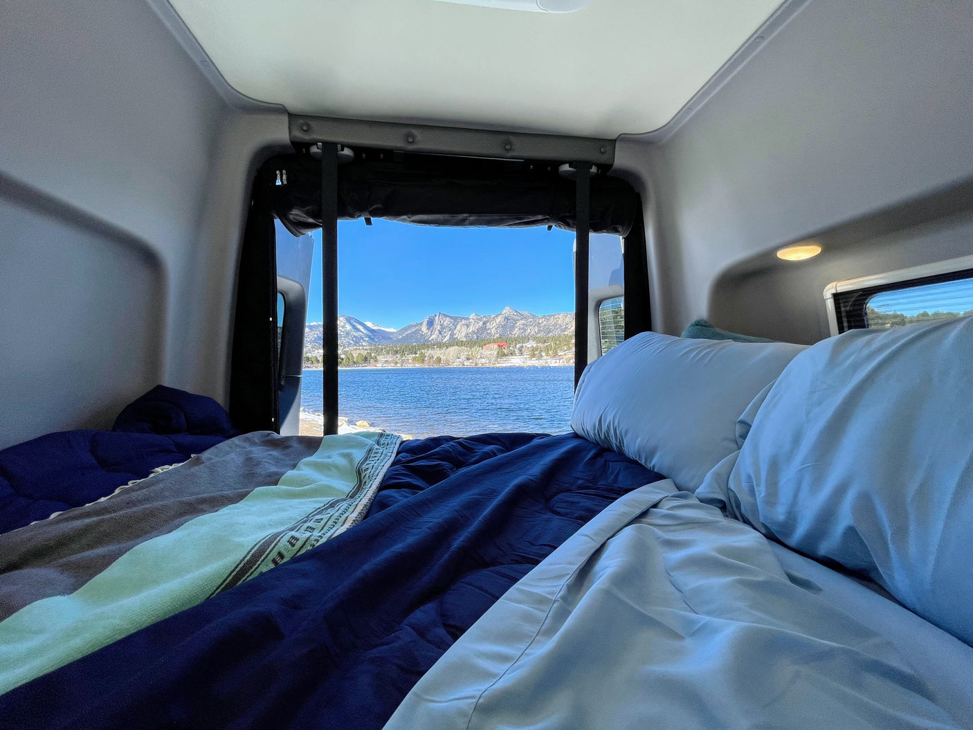 Cozy RV rental bed with a stunning lake and mountain view, perfect for a serene road trip adventure.