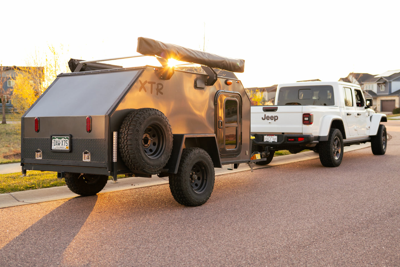 White Jeep Gladiator towing a dark grey XTR off-road teardrop camper, illuminated by warm sunset light for your next RV rental.