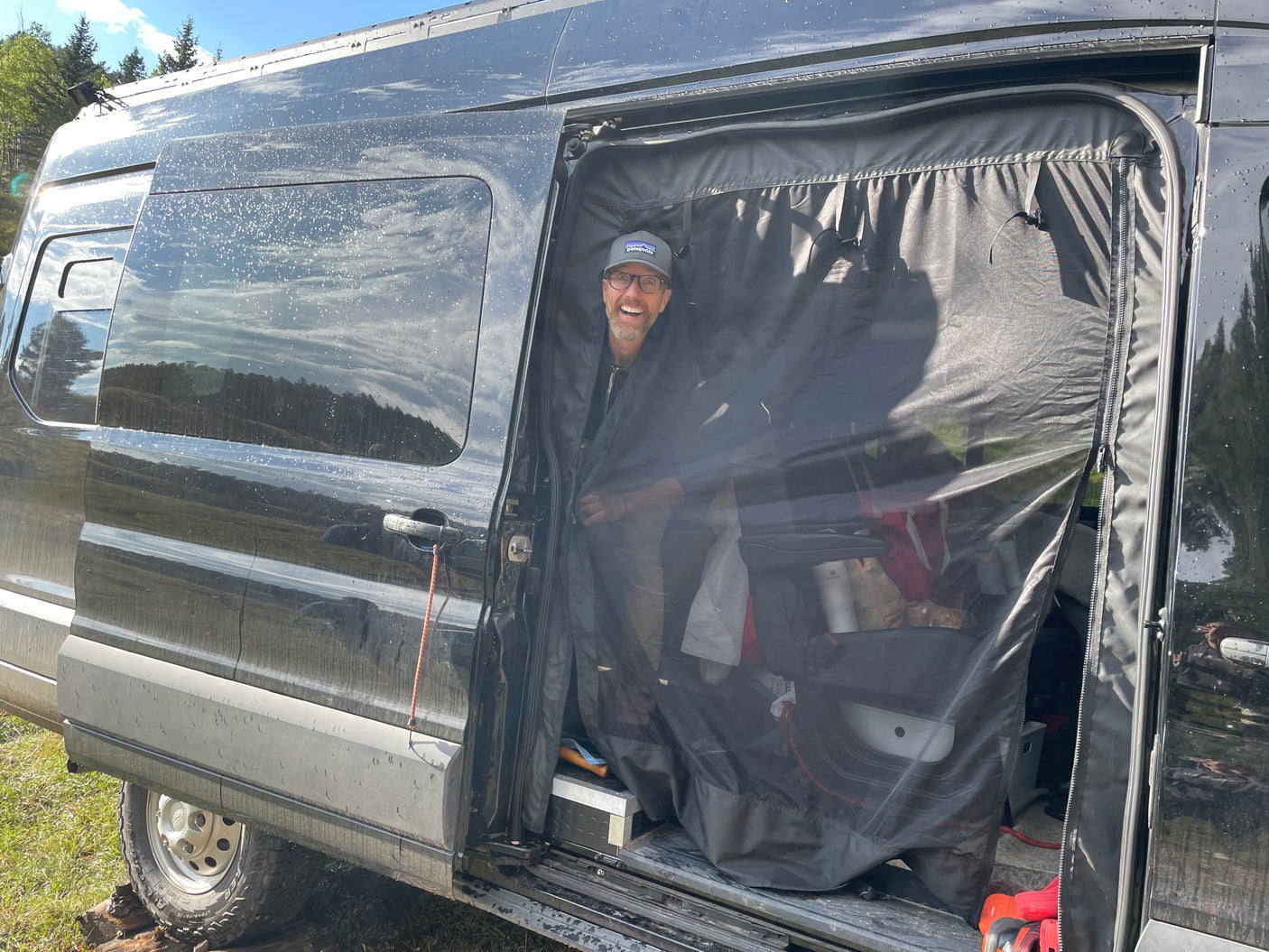 An excited man smiles from his camper van's screened door on an outdoor RV rental trip.
