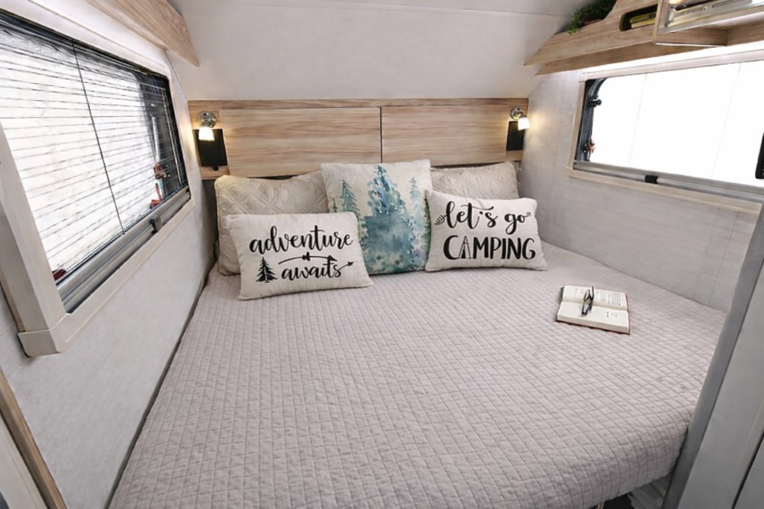 with lights glowing inside.|Inside a comfortable RV rental: a neatly made bed with camping-themed pillows