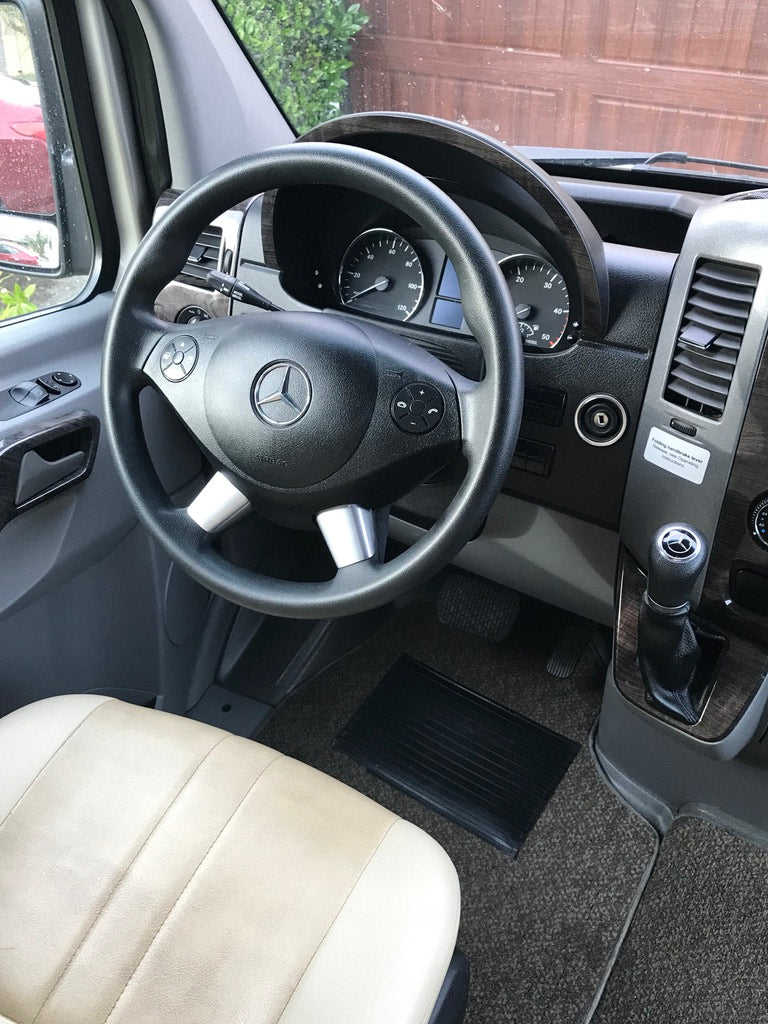 Inside a Mercedes-Benz RV rental, showing the driver's cabin with the steering wheel, dashboard, and light-colored seat.