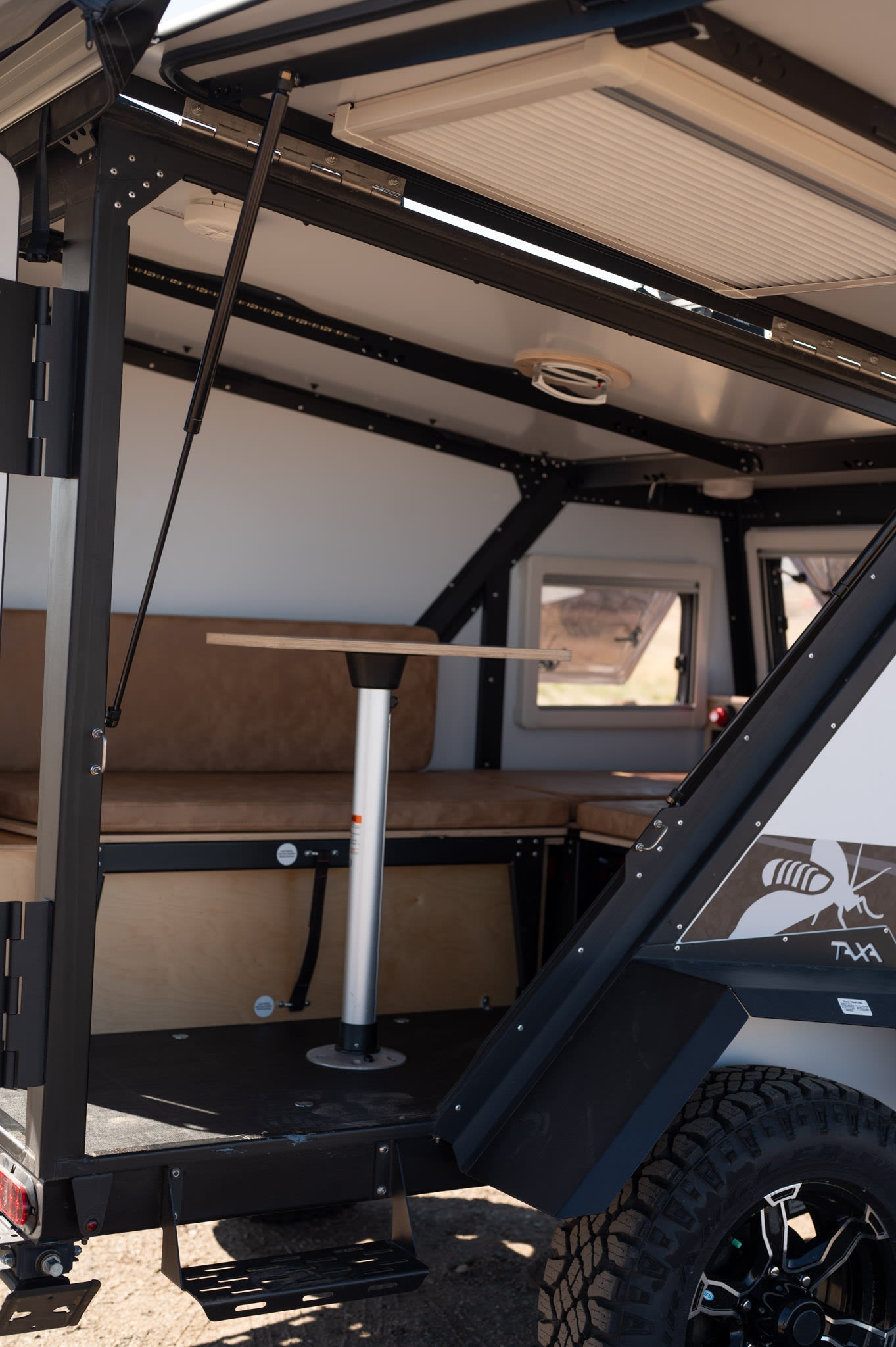 Explore this RV rental camper's interior: a cozy dinette with tan cushions, central table, & bright windows for adventure.