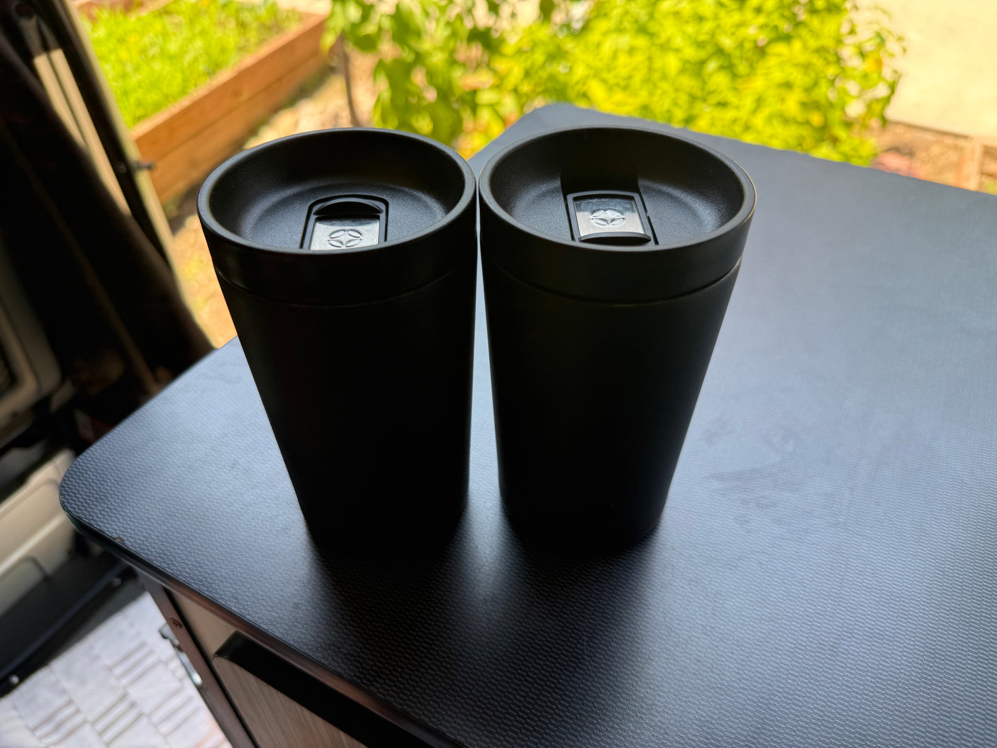 Two black travel mugs on a dark, textured table inside an RV rental, ready for any road trip.