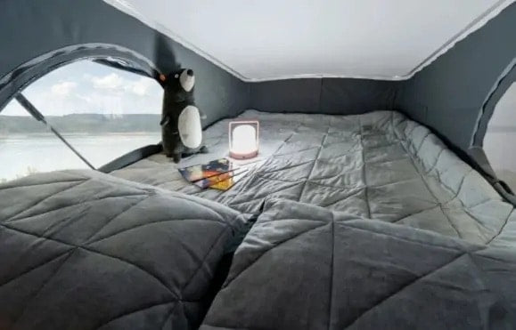 Inside a comfortable RV rental pop-top: a quilted bed, plush toy, glowing lamp, and a stunning lake view. — photo 10