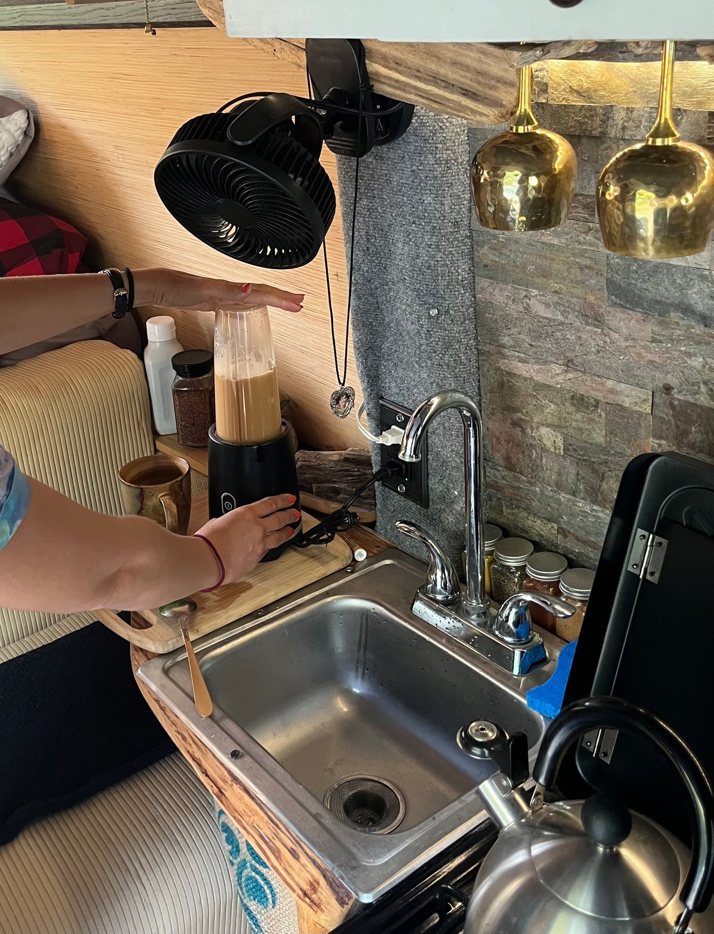 Hands blend a drink in a compact RV rental kitchen, featuring a sink, small appliances, and cozy details for travel.