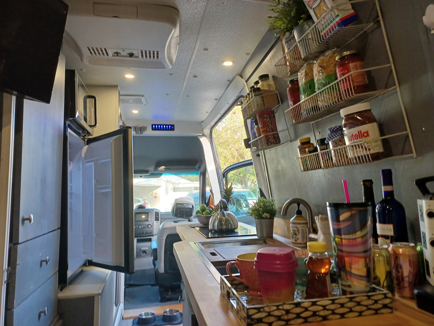 Explore this cozy RV rental's kitchen! It has organized food shelves, a sink, open fridge, and even pet bowls for furry friends.
