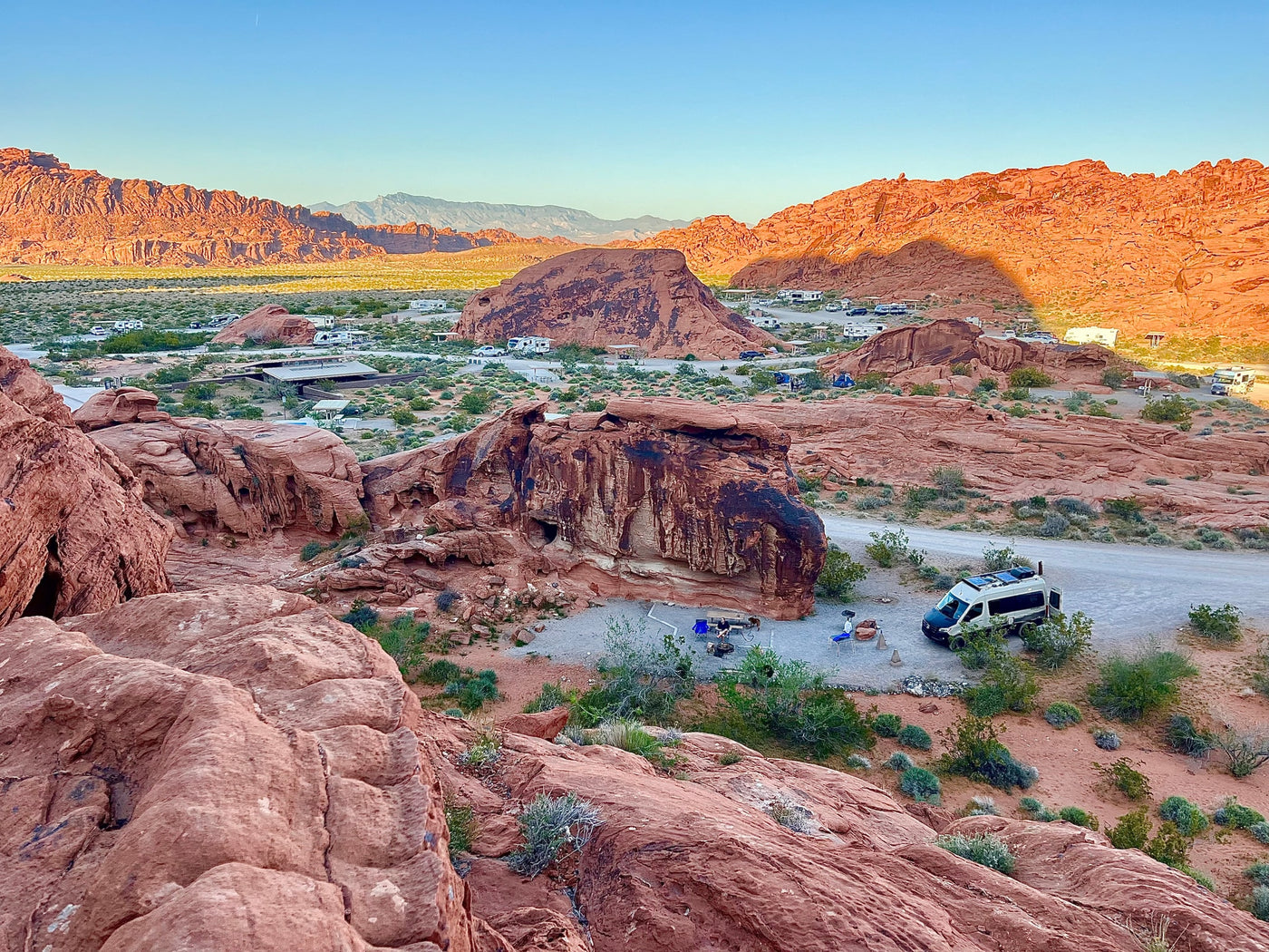 Elevated view of a stunning desert campground with red rock formations, featuring an RV rental and other vehicles. — photo 8
