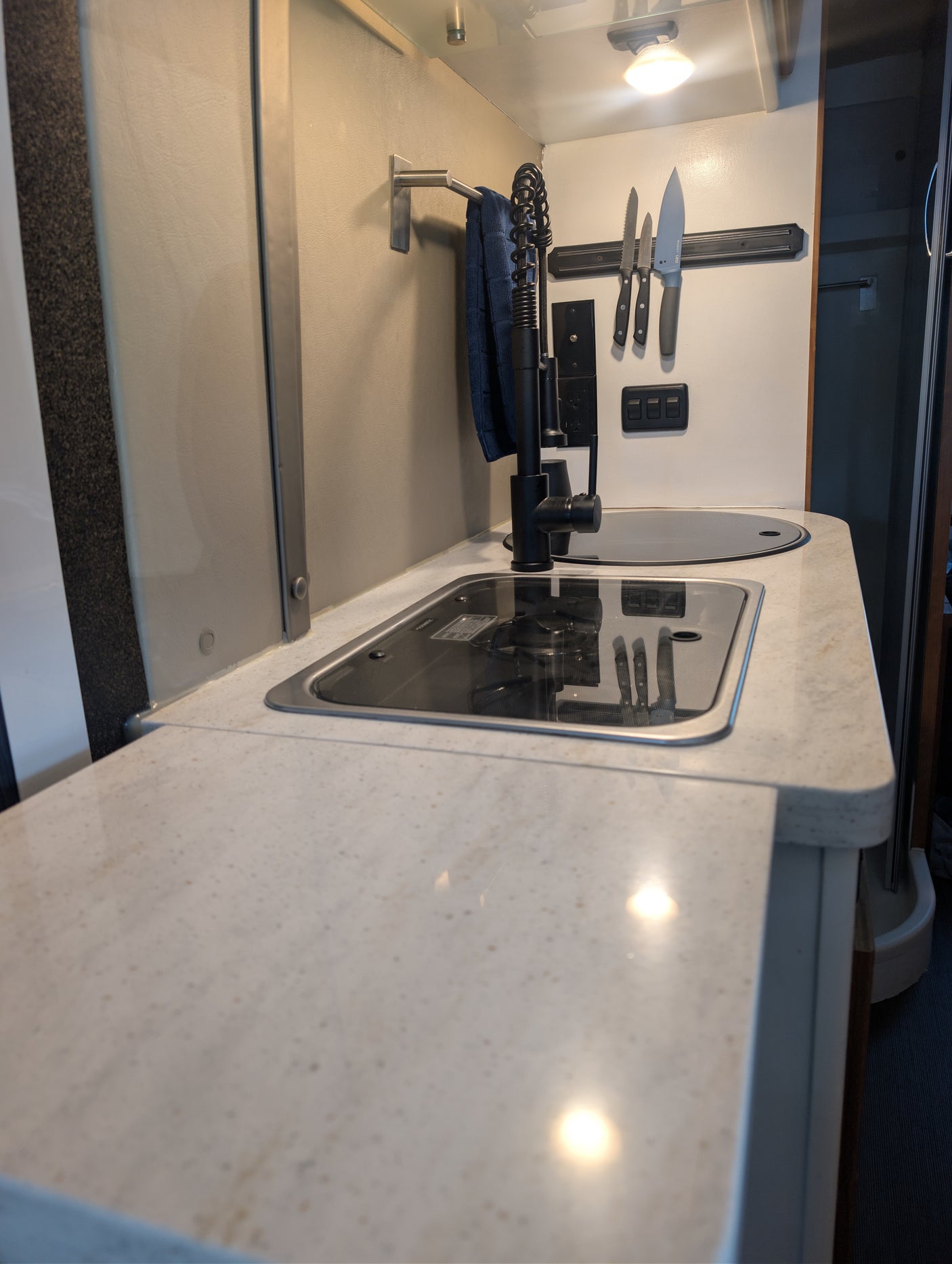 Modern RV rental kitchenette featuring a light-colored countertop, sink, covered stove, and magnetic knife strip.