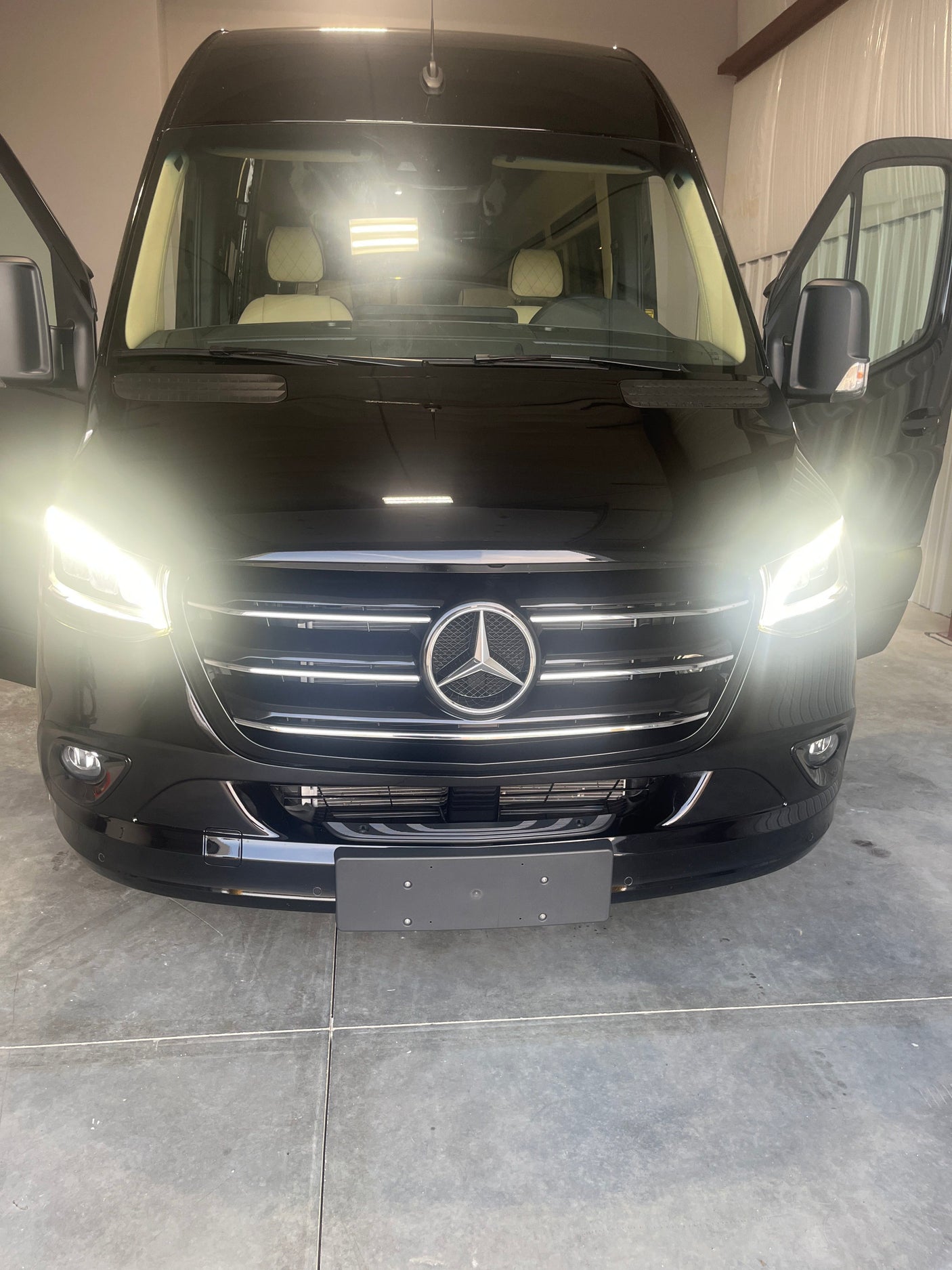 Black Mercedes-Benz Sprinter luxury van ready for **rv rental** adventures. Bright headlights, open doors, plush interior.