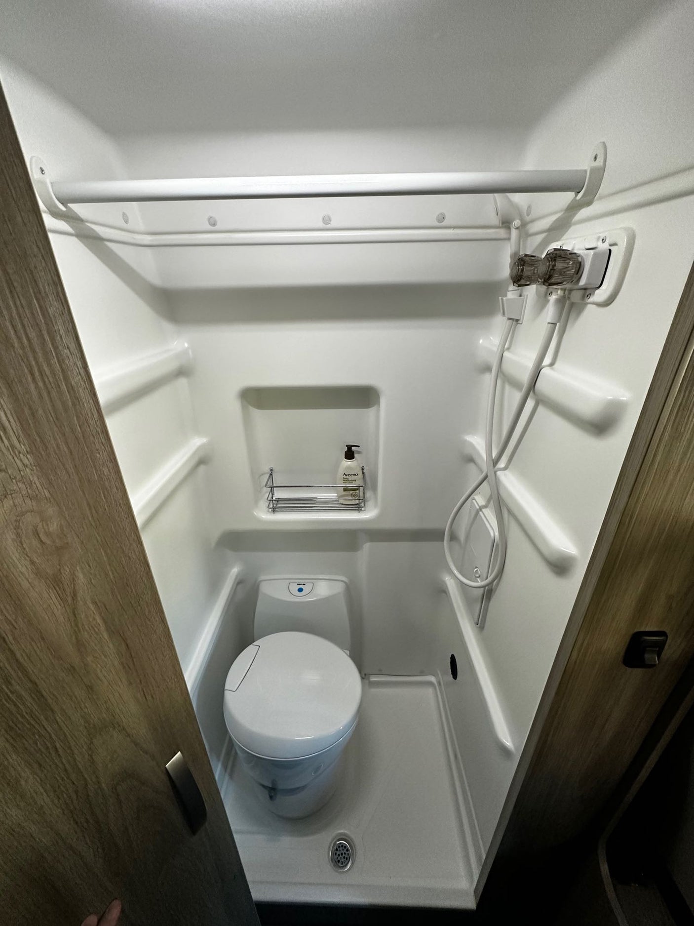 Inside a compact RV rental wet bath, featuring a toilet, shower, and overhead hanging bar. All-in-one convenience.