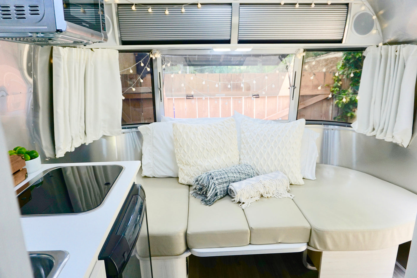 Inside an RV rental: a bright, comfortable living space with a kitchen, curved seating/bed, and charming string lights.