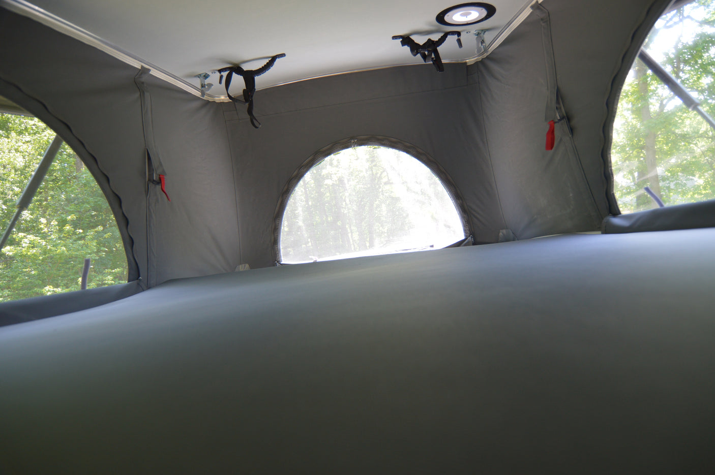 Inside an RV rental pop-top camper's sleeping area with a bed, windows, and light fixture, surrounded by nature.