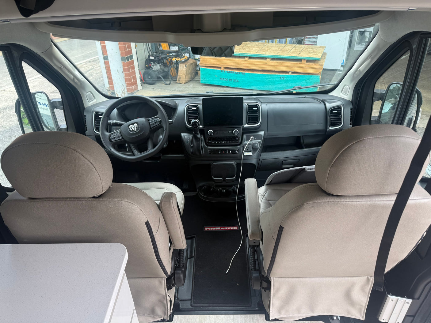 Front interior of an RV rental van: Ram ProMaster cockpit with a modern dashboard, steering wheel, and two light-colored front seats.