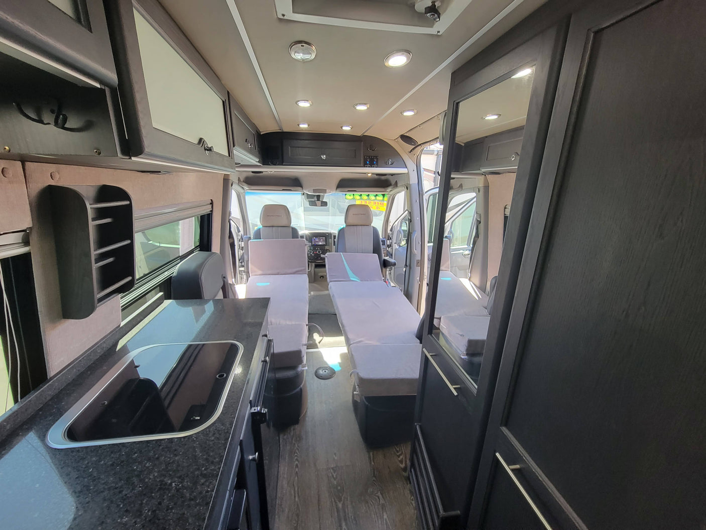 Spacious RV rental interior: a camper van with a kitchenette, convertible seating, overhead storage, and wood floors.