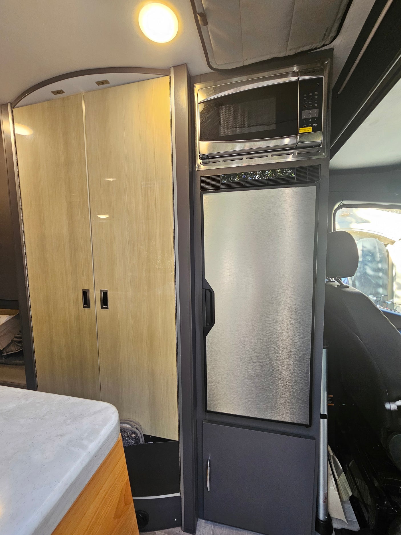 RV rental interior: Features a ceiling light, light wood cabinets, stainless steel microwave, and compact fridge.