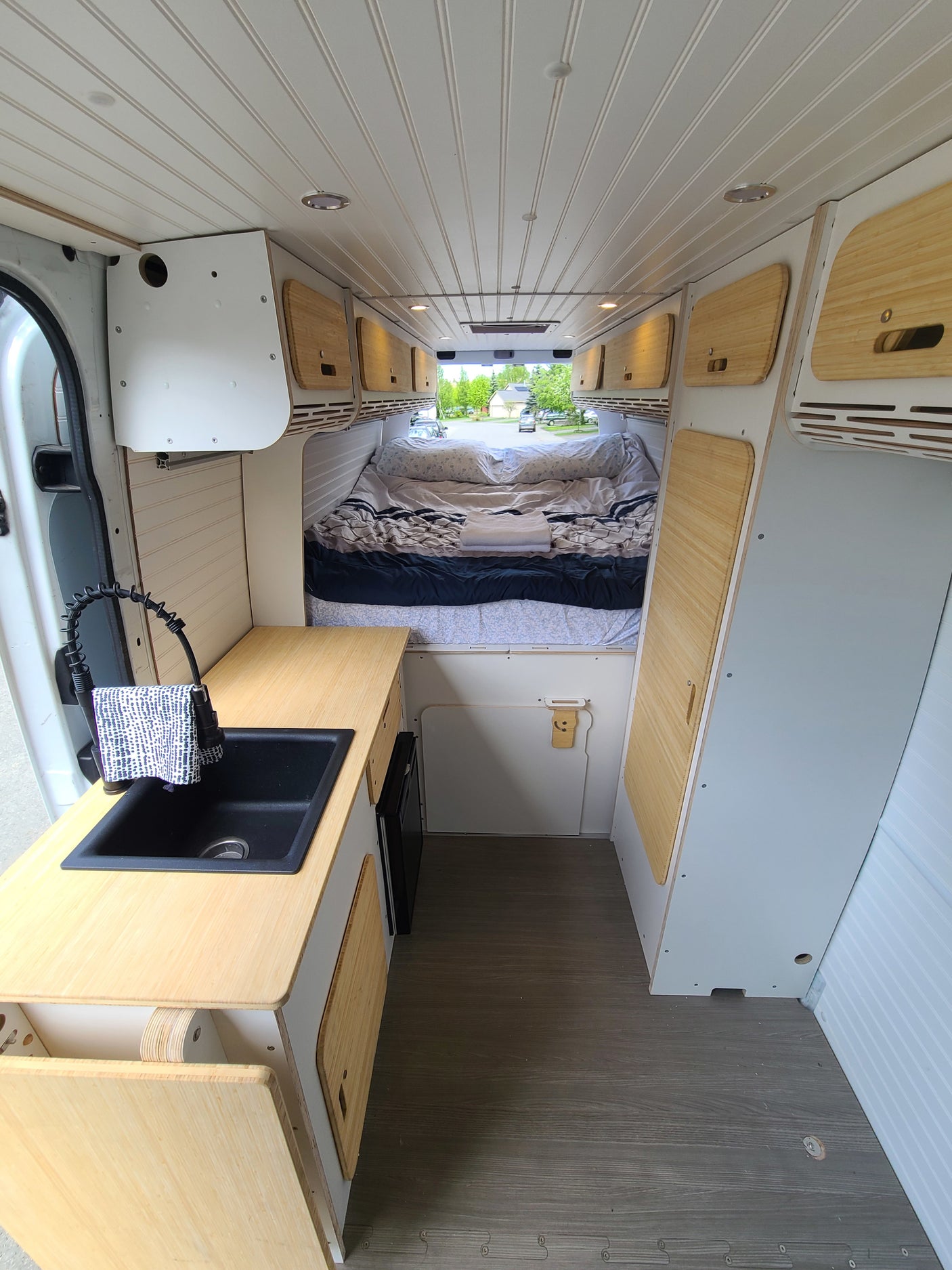 Cozy RV rental interior: Full view of kitchen, bed, and storage in a custom camper van.