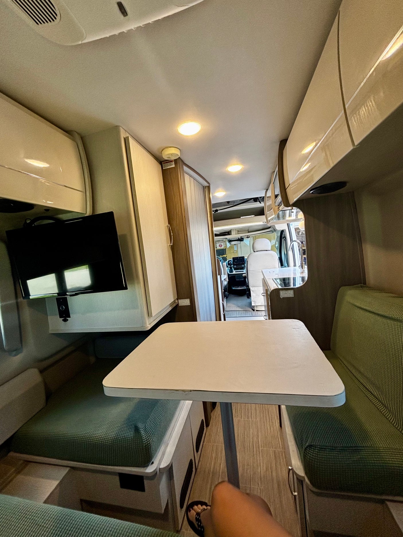 RV rental dinette, TV, and kitchenette in a bright, modern camper van interior.