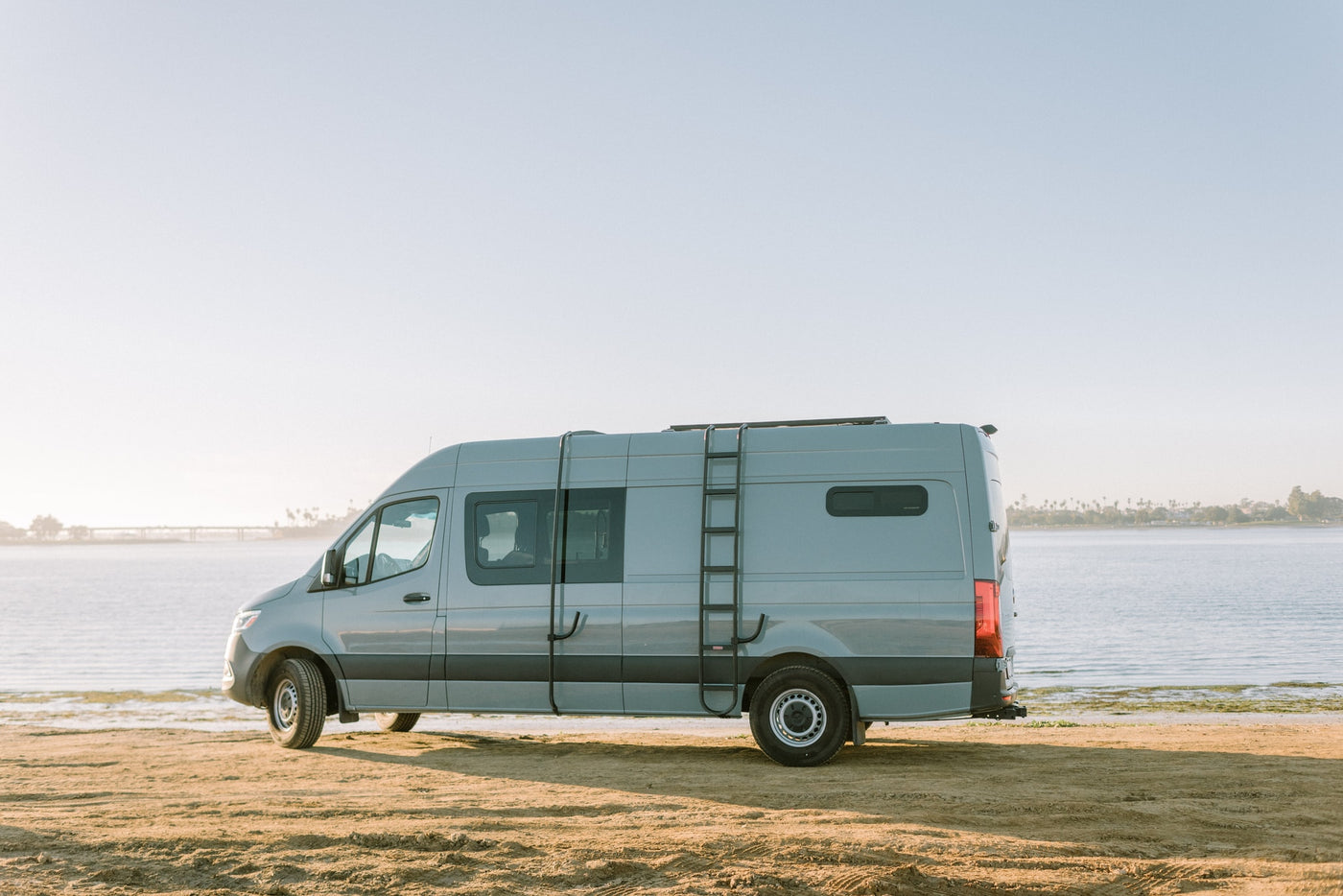 Experience freedom with this RV rental. A grey camper van overlooks a calm waterfront from a sandy beach. — photo 22