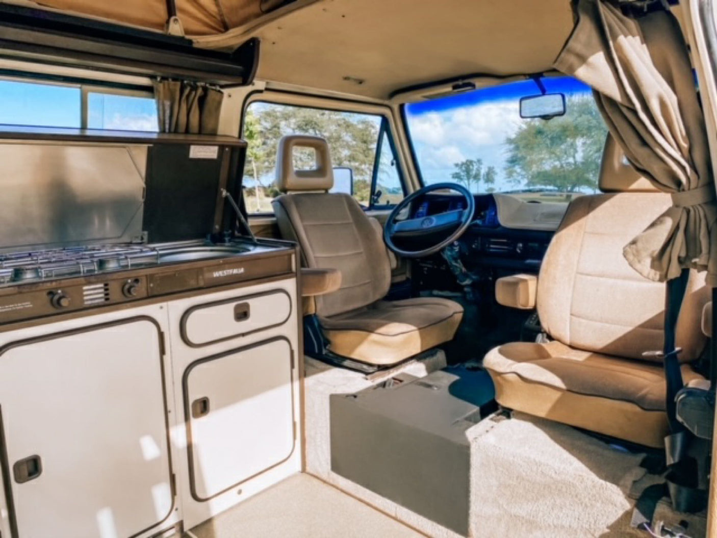 Explore this clean RV rental interior! Features a compact kitchen, comfy tan seats, and a bright cabin view.