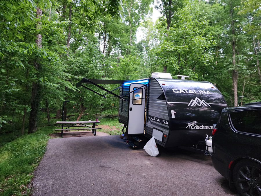 RV rental parked at a lush, green campsite with an extended awning and picnic table. Ideal for outdoor adventures.