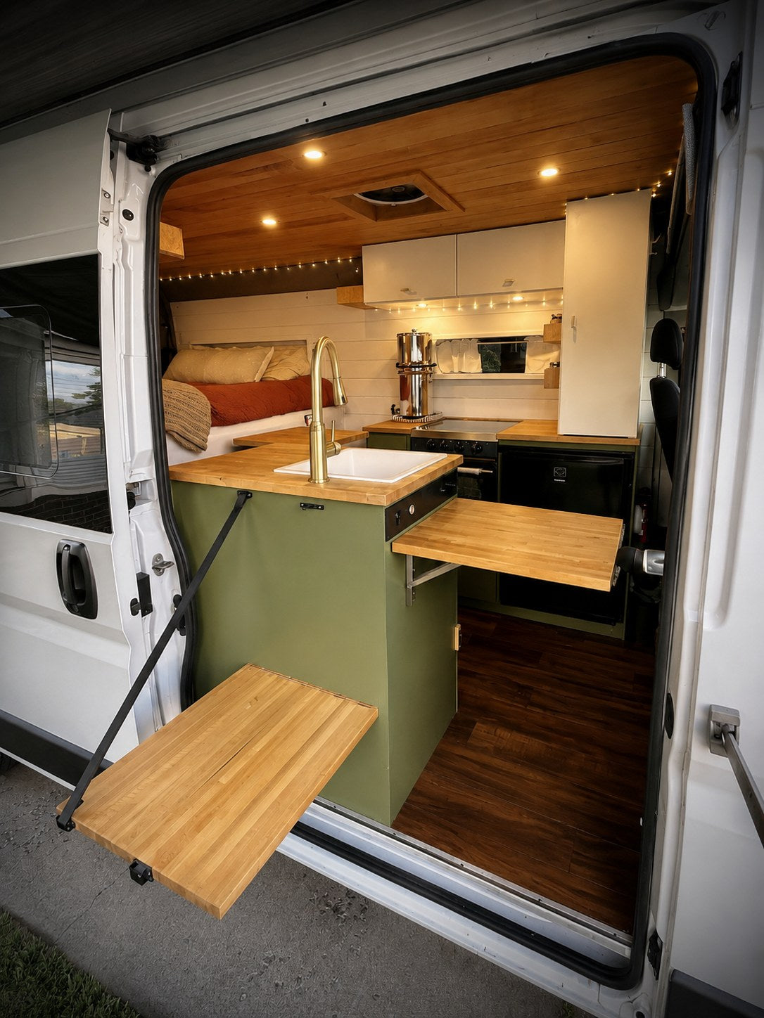 Inside a stylish RV rental camper van: compact kitchen with sink, stove, fridge, fold-out tables, and comfy bed.