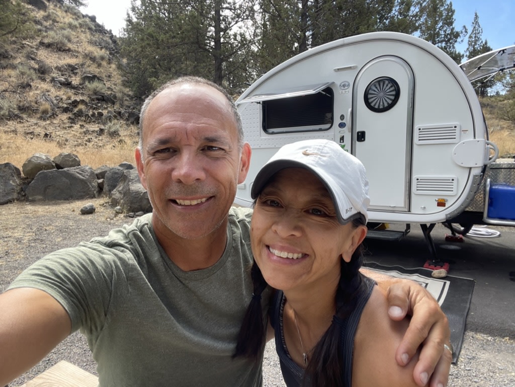 A happy couple poses with their teardrop RV rental at a dry
