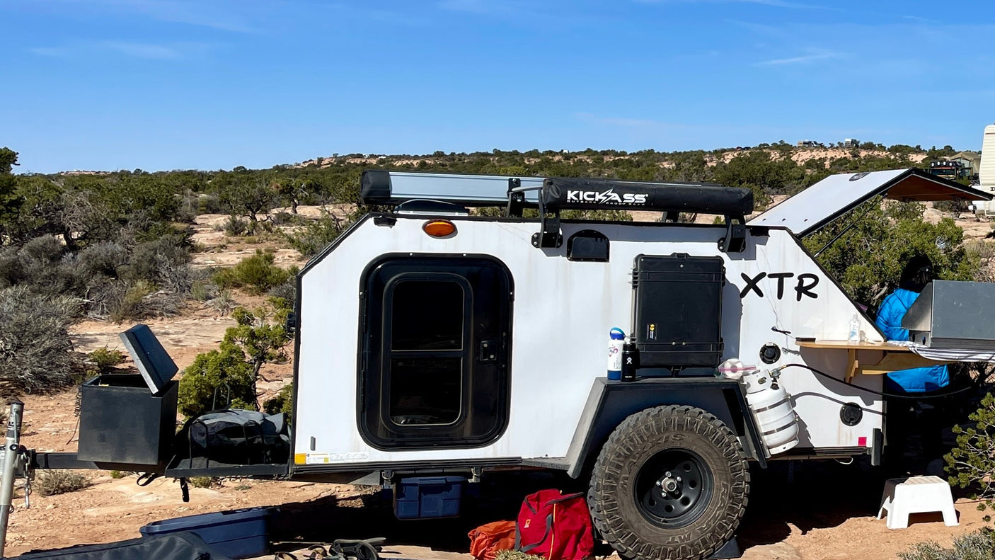 An XTR off-road teardrop trailer, ideal for an RV rental, is set up for camping in a rugged desert environment.