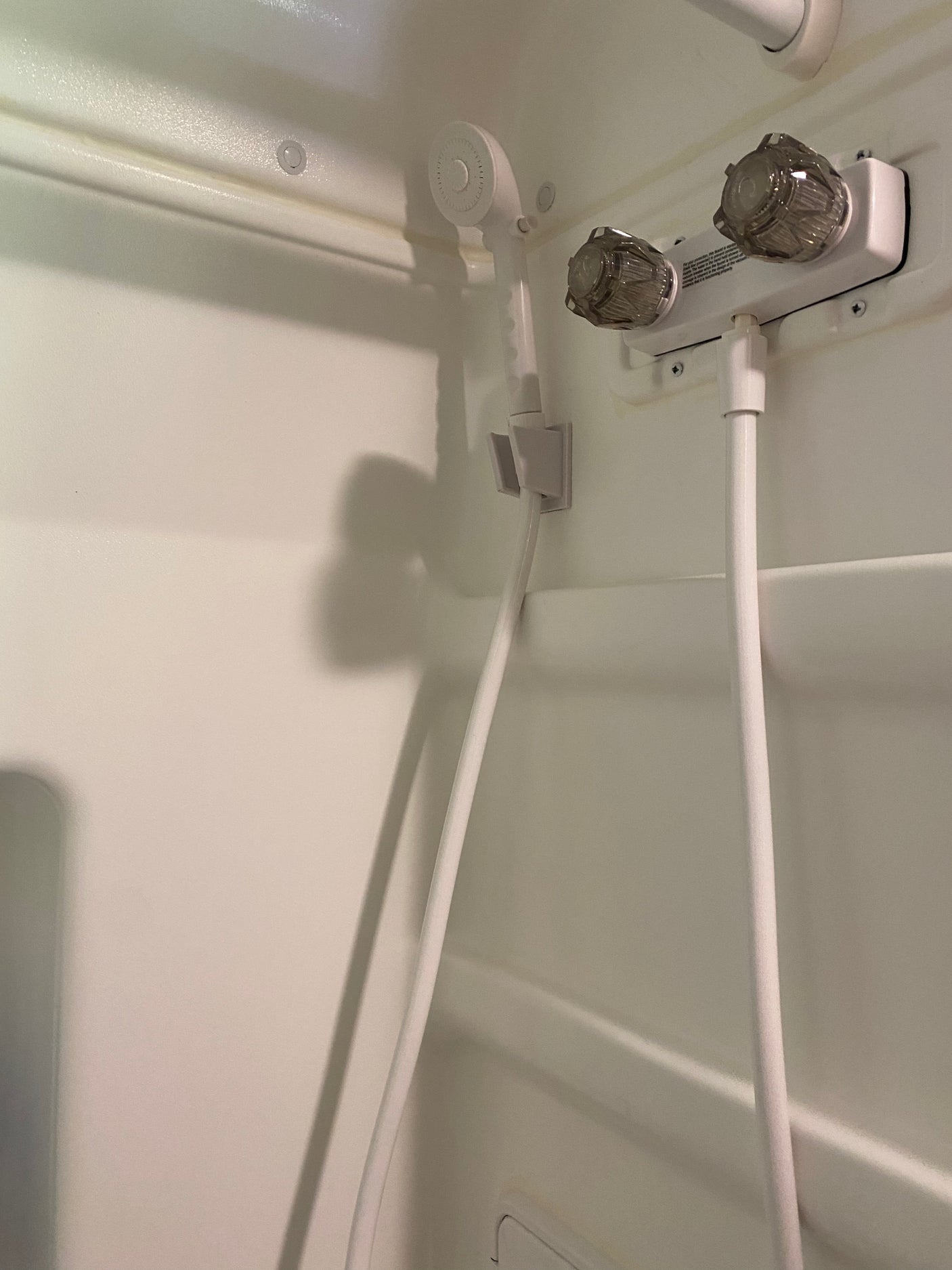 RV rental: Interior white shower with handheld showerhead, hose, and two clear knob water controls.