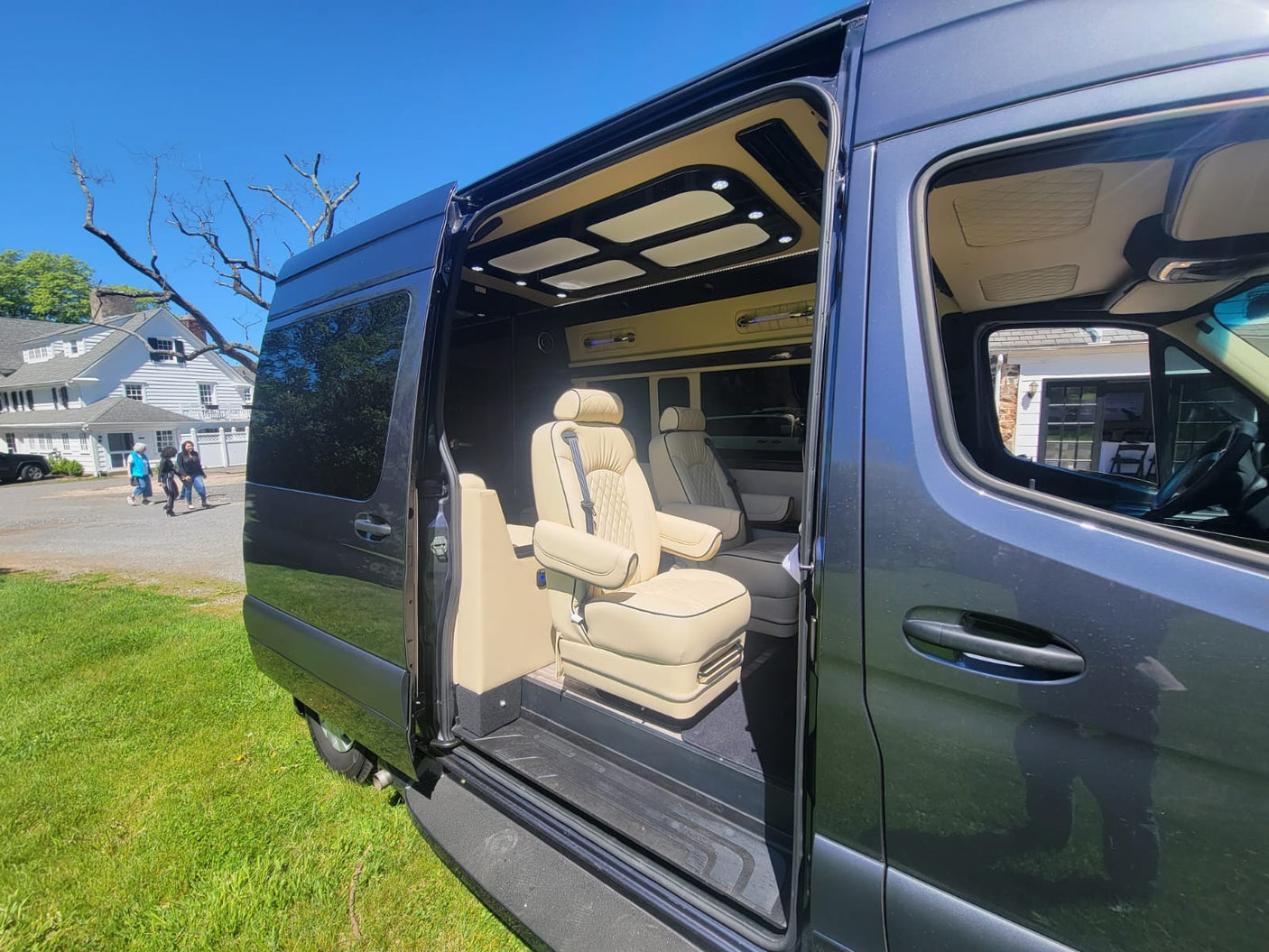 Luxury dark grey RV rental with open side door revealing a lavish tan leather interior, custom captain's chairs, and ambient lighting.