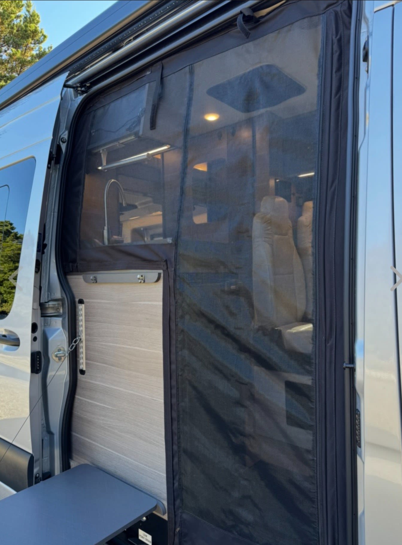 An RV rental's side door with an installed mesh screen, revealing the interior kitchen and a convenient pull-out table.