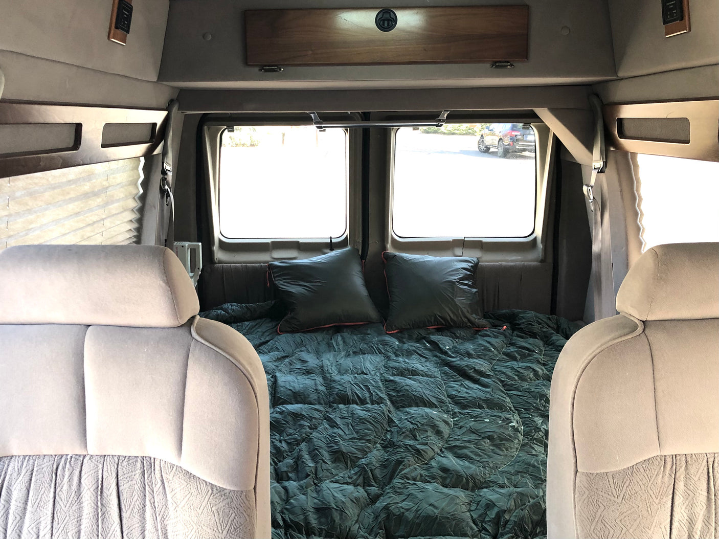 Step inside this cozy RV rental's camper van interior, featuring a comfortable bed, pillows, and bright windows for mobile travel.