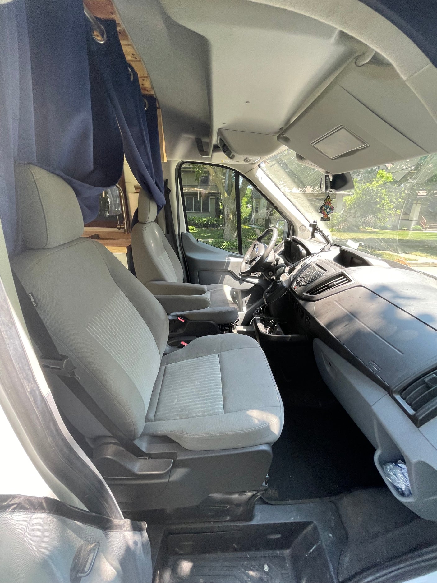 Inside an RV rental van: driver & passenger seats, dashboard, & steering wheel. Blue curtains separate the front cabin from the living area.