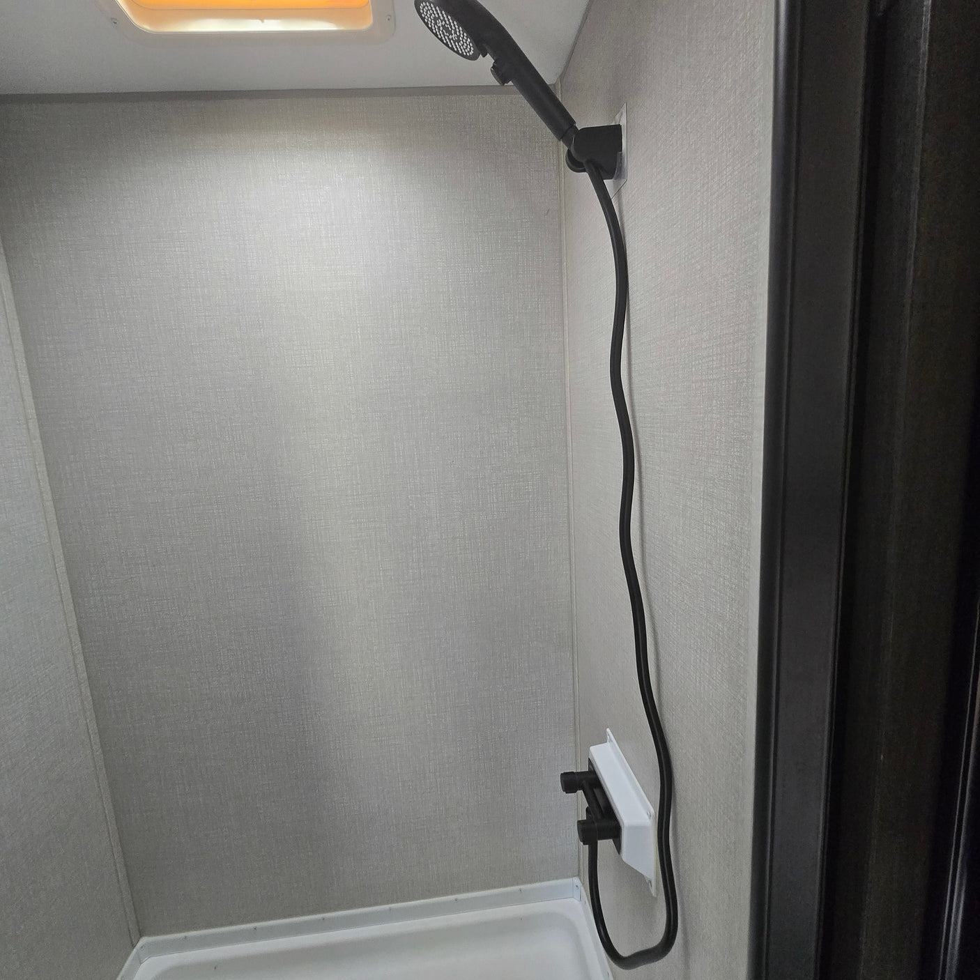 RV rental shower: compact space with light textured walls, white pan, and a black shower head and faucet.