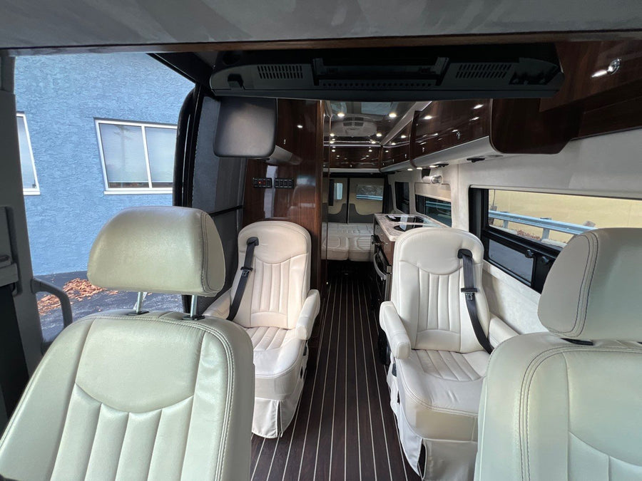 and large windows for scenic rides.|Silver Airstream RV rental parked with its gray awning extended above the open side door.|RV rental: Luxurious van interior with cream leather seating